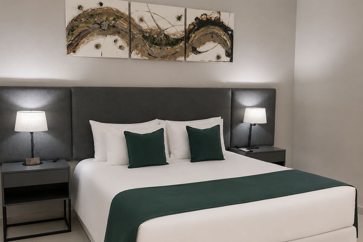 A modern hotel room with a large bed, two bedside tables with lamps, a headboard, and abstract artwork on the wall.
