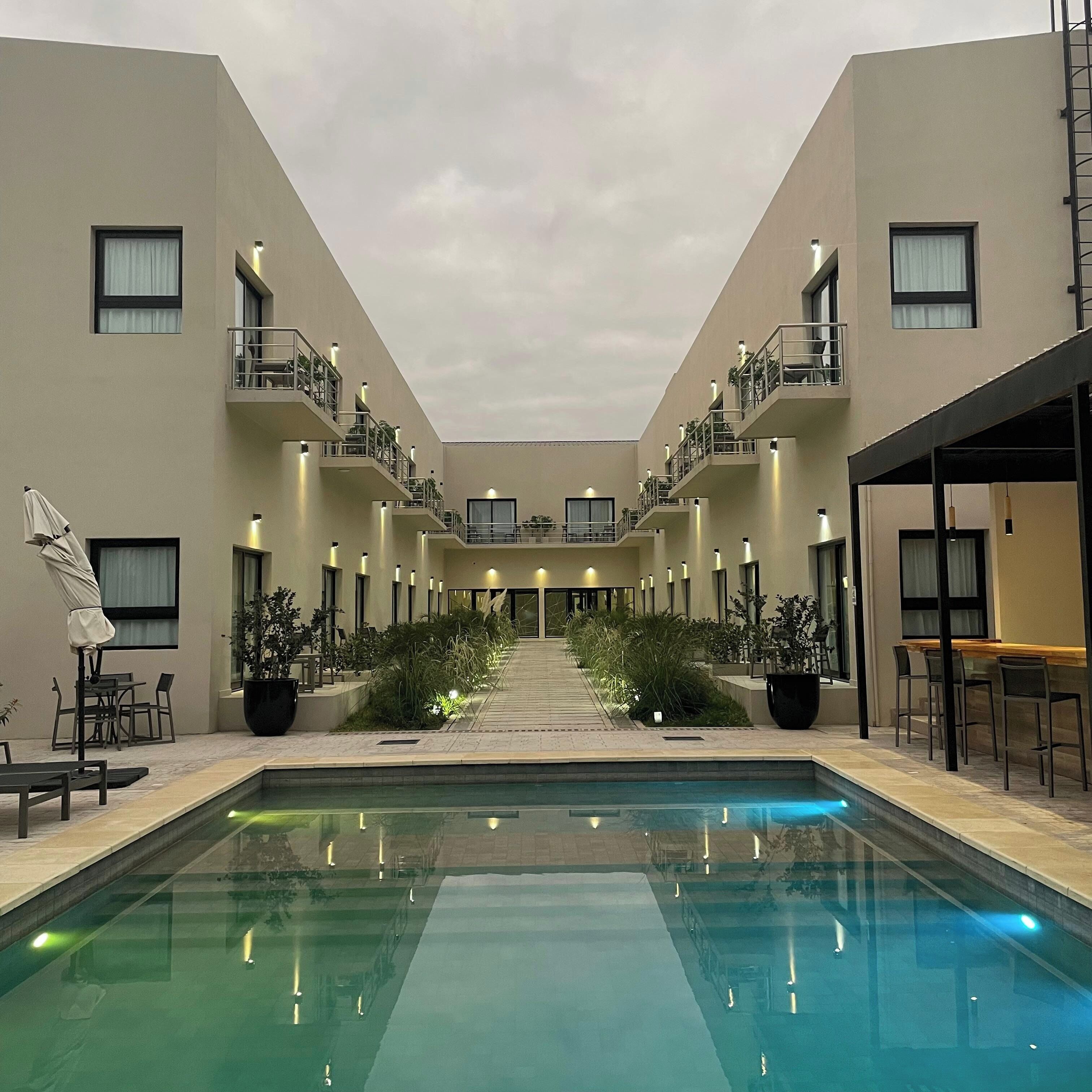 Pátio de hotel com piscina central, mobiliário de exterior e várias varandas.