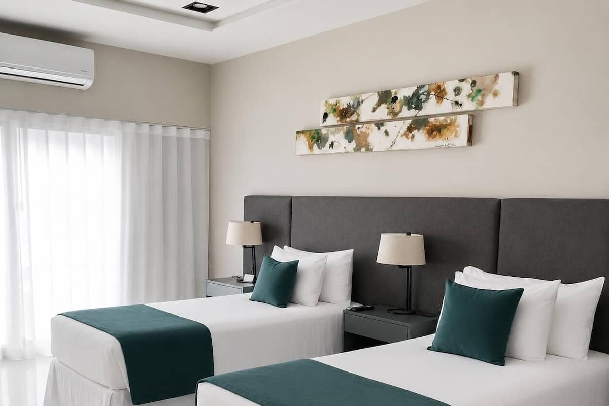 A hotel room with two beds, a large window with curtains, an air conditioning unit, and a wall-mounted artwork.