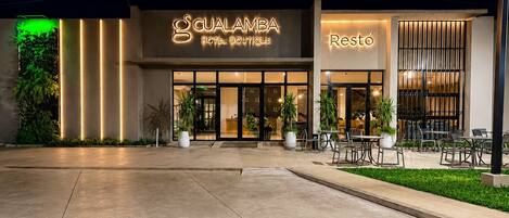 A hotel entrance with a modern design, featuring a prominent sign for 'GUALAMBA HOTEL BOUTIQUE' and a separate section labeled 'Restó'.