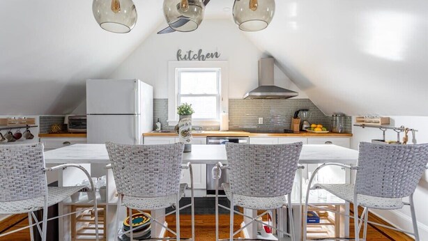 A modern kitchen with a white refrigerator, a stove, and a sink. There are four wicker chairs around a white table. - Renovated 2BR Retreat / Modern Comforts Included (Bridgeport)