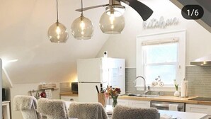 A modern kitchen with a dining area, featuring a white island, bar stools, and pendant lighting. - Renovated 2BR Retreat / Modern Comforts Included (Bridgeport)