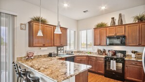 A modern kitchen with granite countertops, wooden cabinets, a built-in oven, and a large island with bar stools. - Cozy Granville Retreat W/ Modern Amenities 3 Bedroom Home (Prescott Valley)