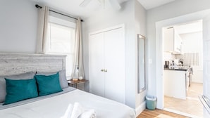 Un dormitorio con cama, mesita de noche, ventilador de techo, armario y vista a la cocina.