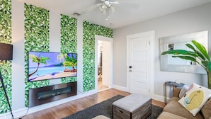 Una sala de estar con televisión, ventilador de techo, sofá y una planta grande.