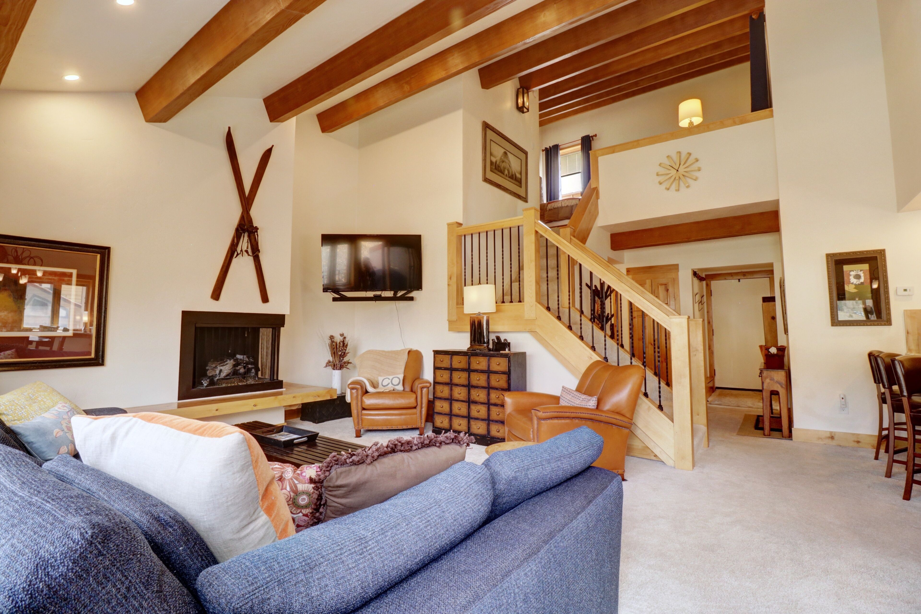 Un salon spacieux avec un grand canapé bleu, un escalier en bois, une télévision et une cheminée.