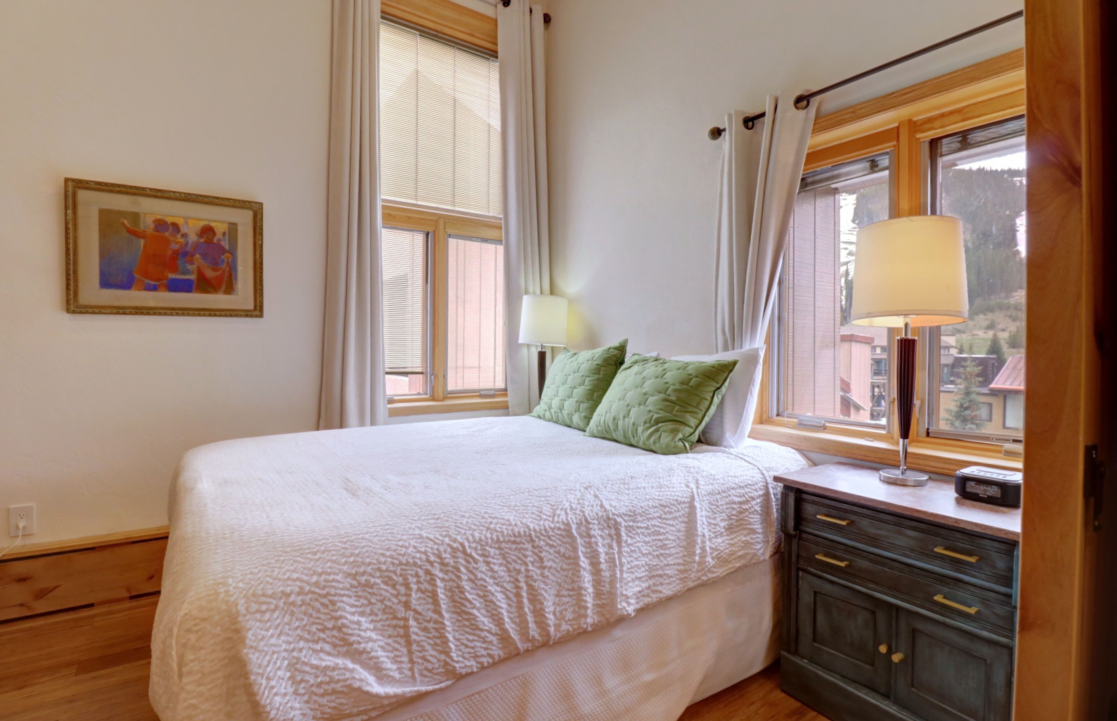 Une chambre à coucher avec un lit, une table de chevet, une lampe et une fenêtre avec des rideaux.