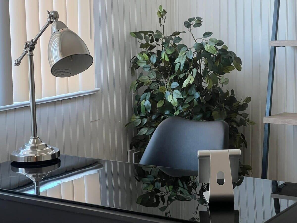 Een modern bureau met een metalen bureaulamp, een potplant en een stoel.