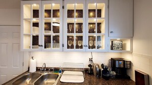 A modern kitchen with white cabinetry, a dish drying rack, a coffee maker, and a sign stating "Education is important but coffee is importanter." - The Blue Sapphire: Modern & Stylish 2BR w/ 2 King Beds & Full Kitchen (Bridgeport)