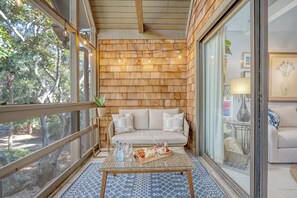 Una habitación acogedora con pared de madera, un sofá, una mesita de centro con una bandeja de aperitivos y vistas a árboles.