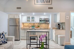 Cocina moderna con armarios blancos, electrodomésticos de acero inoxidable, salpicadero de azulejos y una isla central con taburetes.