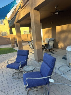 Eine Außenpatio-Terrasse mit blauen, gepolsterten Stühlen und einem kleinen Tisch, gestützt von Betonpfeilern.