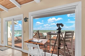 A room with a large window overlooking the beach, a table with a camera on a tripod, and a hammock outside. - Aquarius Oceanside: 9BR/8BA Beachfront w/ Pool, Hot Tub, Elevator & Riverfront (Stuart)