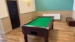 A pool table in a room with wooden flooring, a radiator, and a door. - The Talbot Hotel (Stourbridge)
