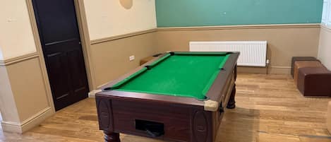 A pool table in a room with wooden flooring, a radiator, and a door.