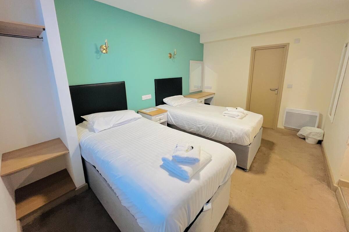 Una habitación de hotel con dos camas, un escritorio pequeño, un espejo y una puerta.