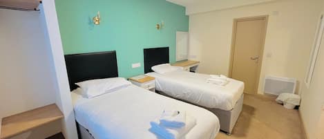 A hotel room with two beds, a small desk, a mirror, and a door.