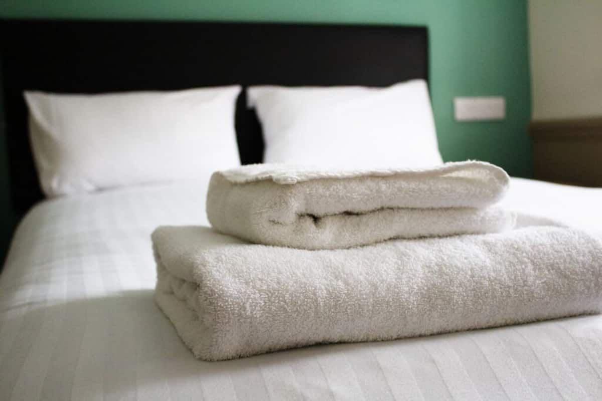 Una cama bien hecha con sábanas blancas y una toalla blanca doblada encima.