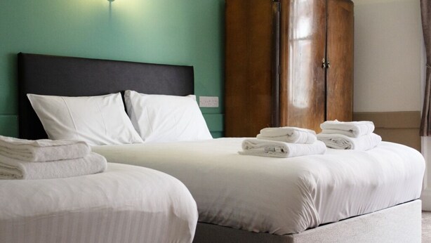 A hotel room with two beds, a wardrobe, and a wall-mounted light fixture. - The Talbot Hotel (Stourbridge)