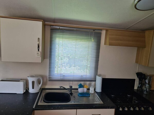 Een kleine keuken met een spoelbak, waterkoker, broodrooster en fornuis.