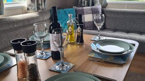 A dining table set with plates, glasses, and bottles, with a view of a balcony and a sofa in the background. - 2 Bed Lodge - Sleeps 6 - Parking - Pets - Wifi (Millom)