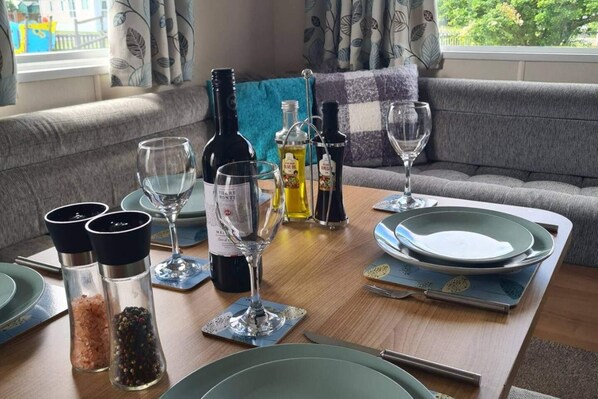 Een eettafel gedekt met borden, glazen en flessen, met zicht op een balkon en een bank op de achtergrond.