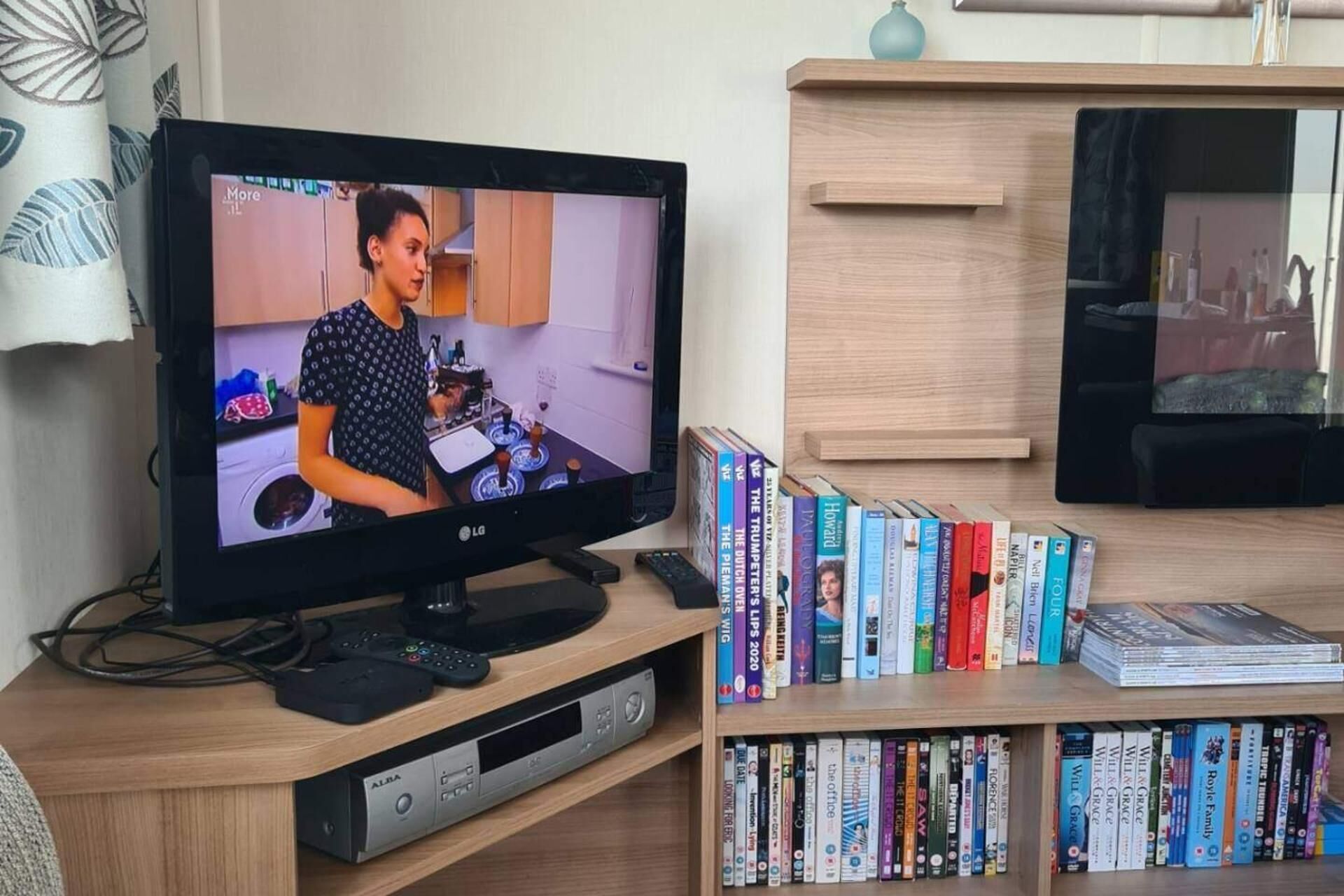 A television displaying a scene, a bookshelf with books, and a remote control on a wooden stand.