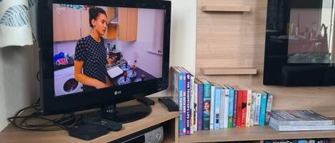 A television displaying a scene, a bookshelf with books, and a remote control on a wooden stand.