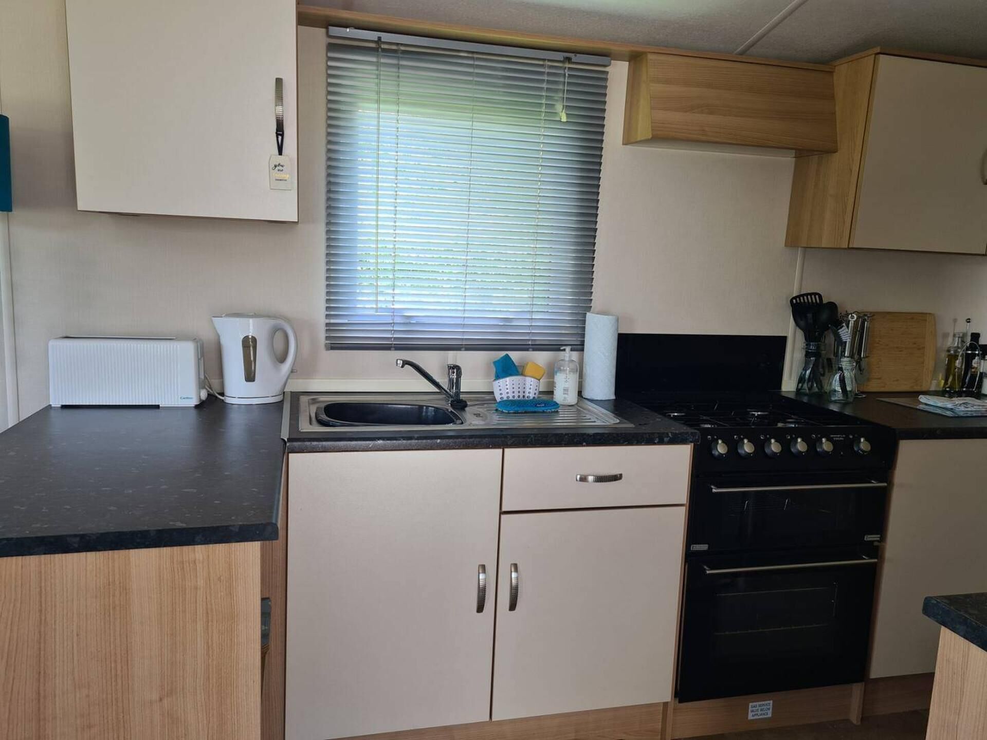A compact kitchen with a gas stove, a kettle, and a sink.
