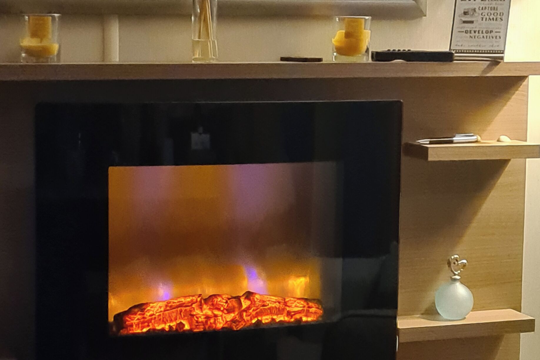 Une cheminée avec un feu visible, une télécommande et un petit objet décoratif posé sur une étagère.