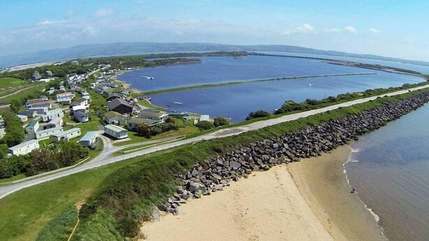 An aerial view of a coastal area with a beach, a row of houses, and a large body of water. - 2 Bed Lodge - Sleeps 6 - Parking - Pets - Wifi (Millom)