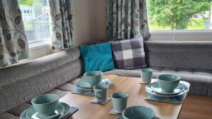 A cozy living room with a sofa, cushions, and a coffee table set with matching blue cups and saucers. - 2 Bed Lodge - Sleeps 6 - Parking - Pets - Wifi (Millom)