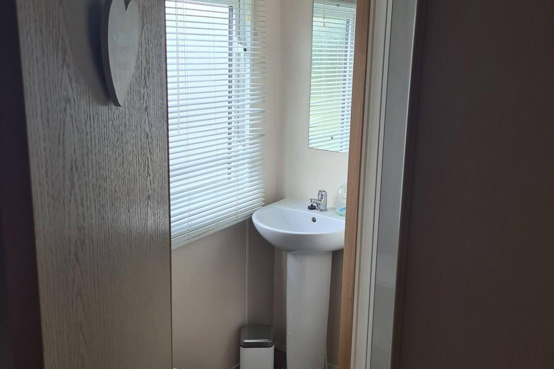A small bathroom with a white sink, a mirror, and a window with blinds.