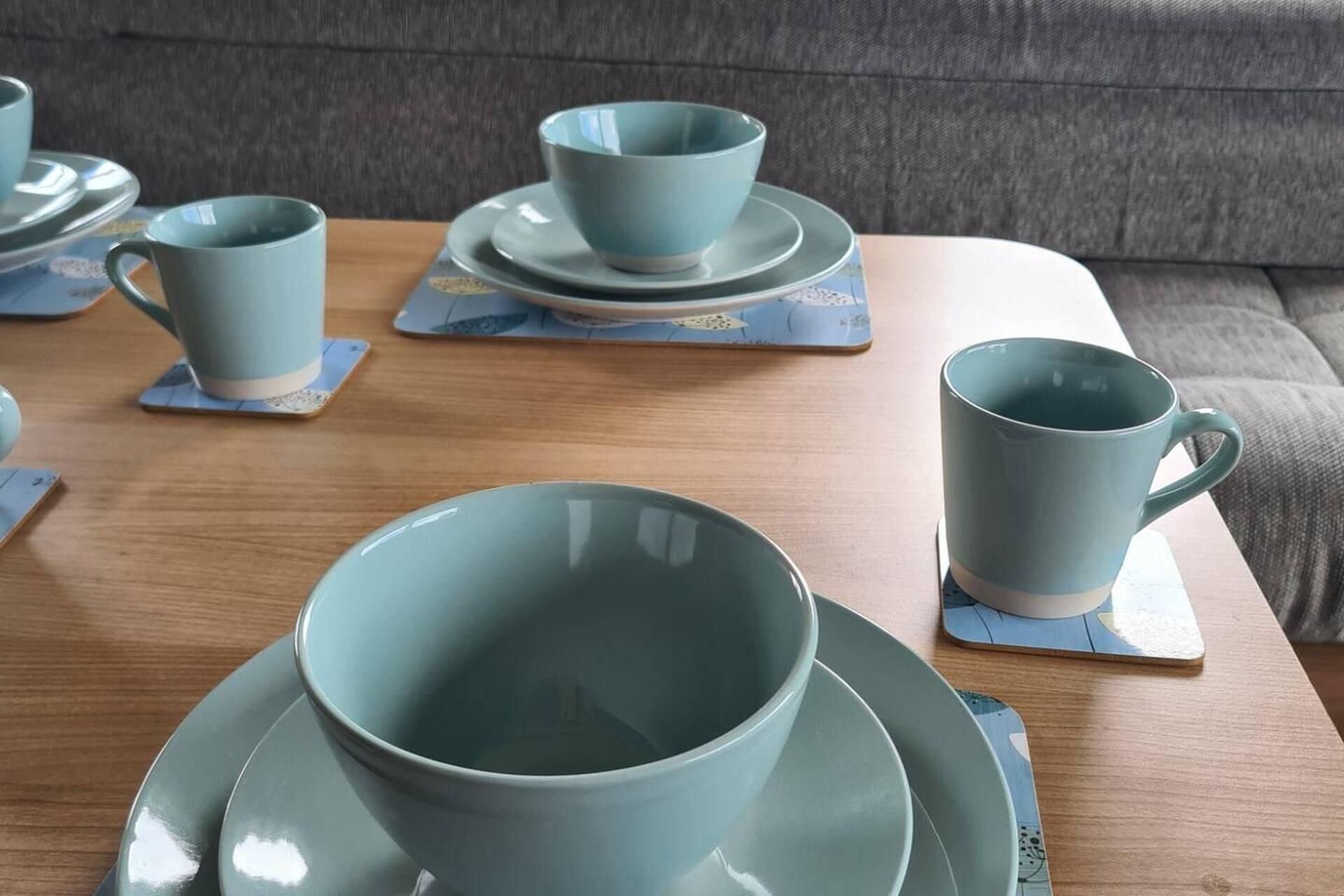 Taula amb conjunt de tasses i platets de color blau marí sobre draparons, disposats sobre una taula de fusta en una habitació amb un sofà gris al fons.