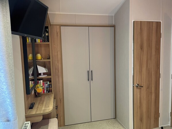 A room with a wardrobe, a television mounted on a wooden shelf, and a door with a handle. - Lavender super front row sea view caravan at Rockley Park, Poole Harbour, Dorset (Poole)