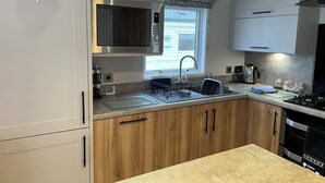 A compact kitchen with a built-in microwave, a sink, and a stove. - Lavender super front row sea view caravan at Rockley Park, Poole Harbour, Dorset (Poole)