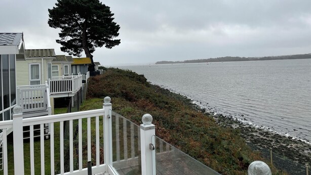 A coastal view with a white fence, a tree, and a body of water. - Lavender super front row sea view caravan at Rockley Park, Poole Harbour, Dorset (Poole)