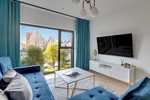 A modern living room with a large window, a sofa, a coffee table, and a TV mounted on the wall.