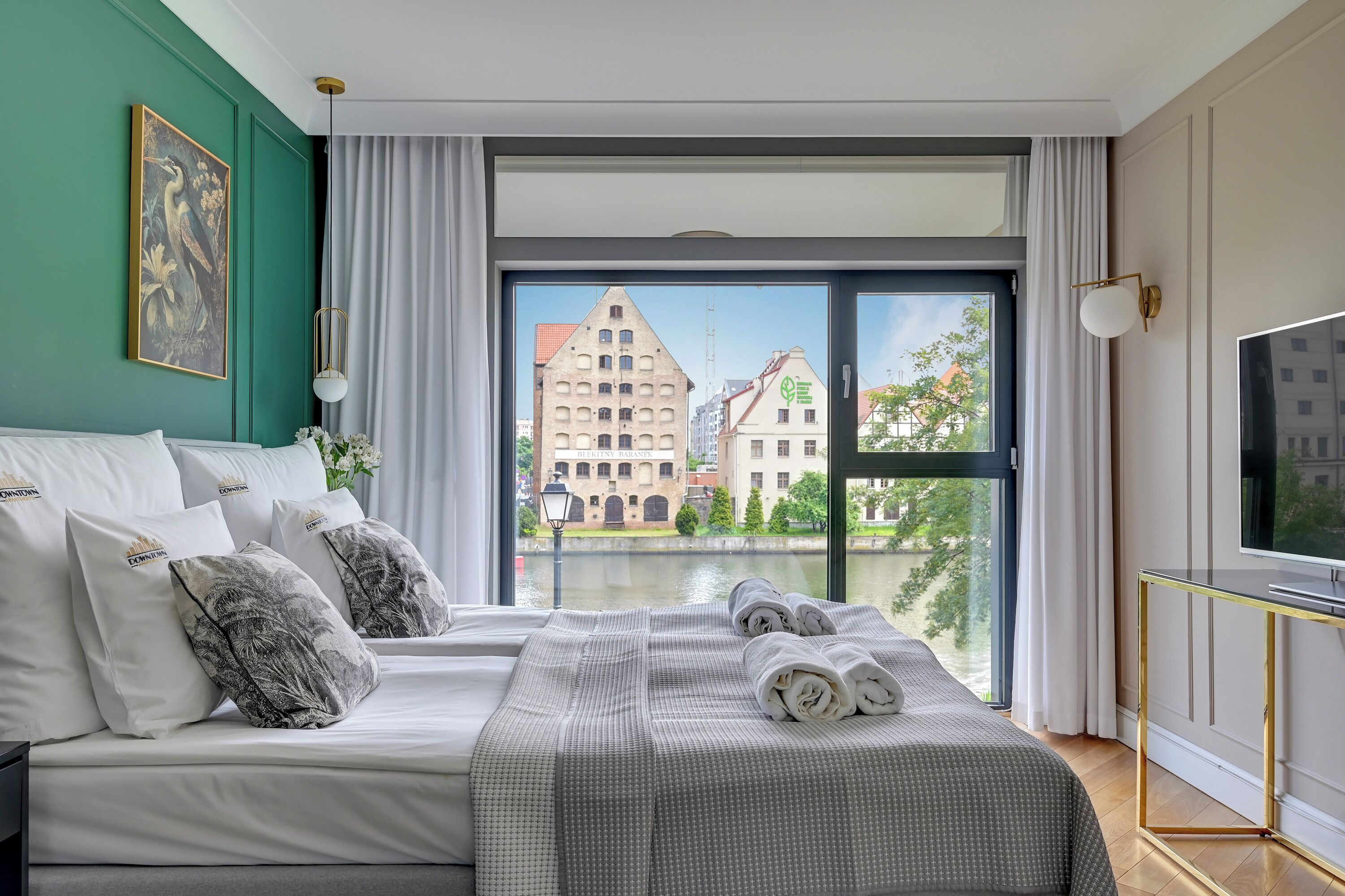 A hotel room with a large bed, a TV, and a view of buildings through the window.