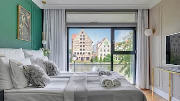 A hotel room with a large bed, a TV, and a view of buildings through the window.