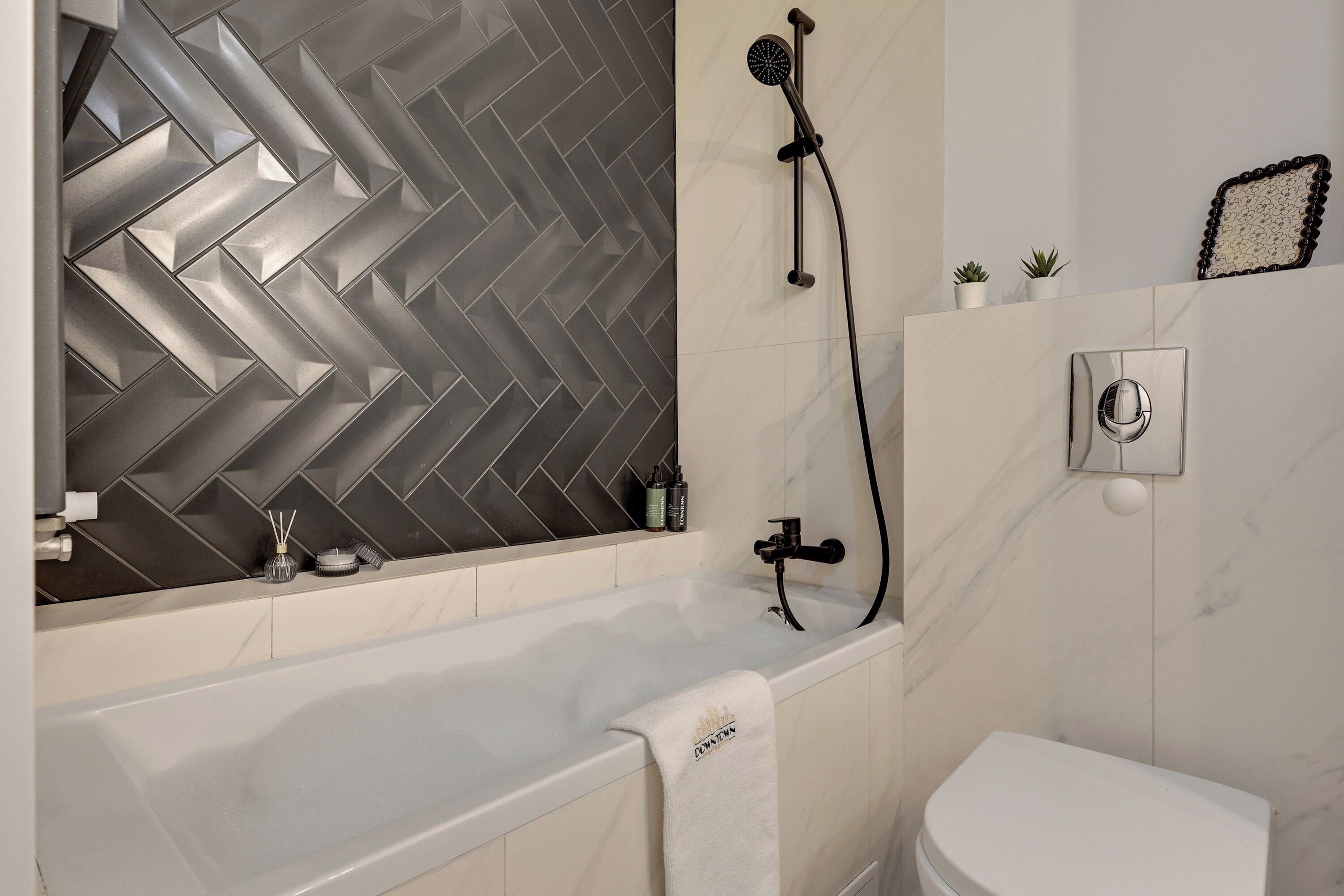 Un baño moderno con pared de diseño en patrón de espiga, una bañera, un inodoro y una ducha.