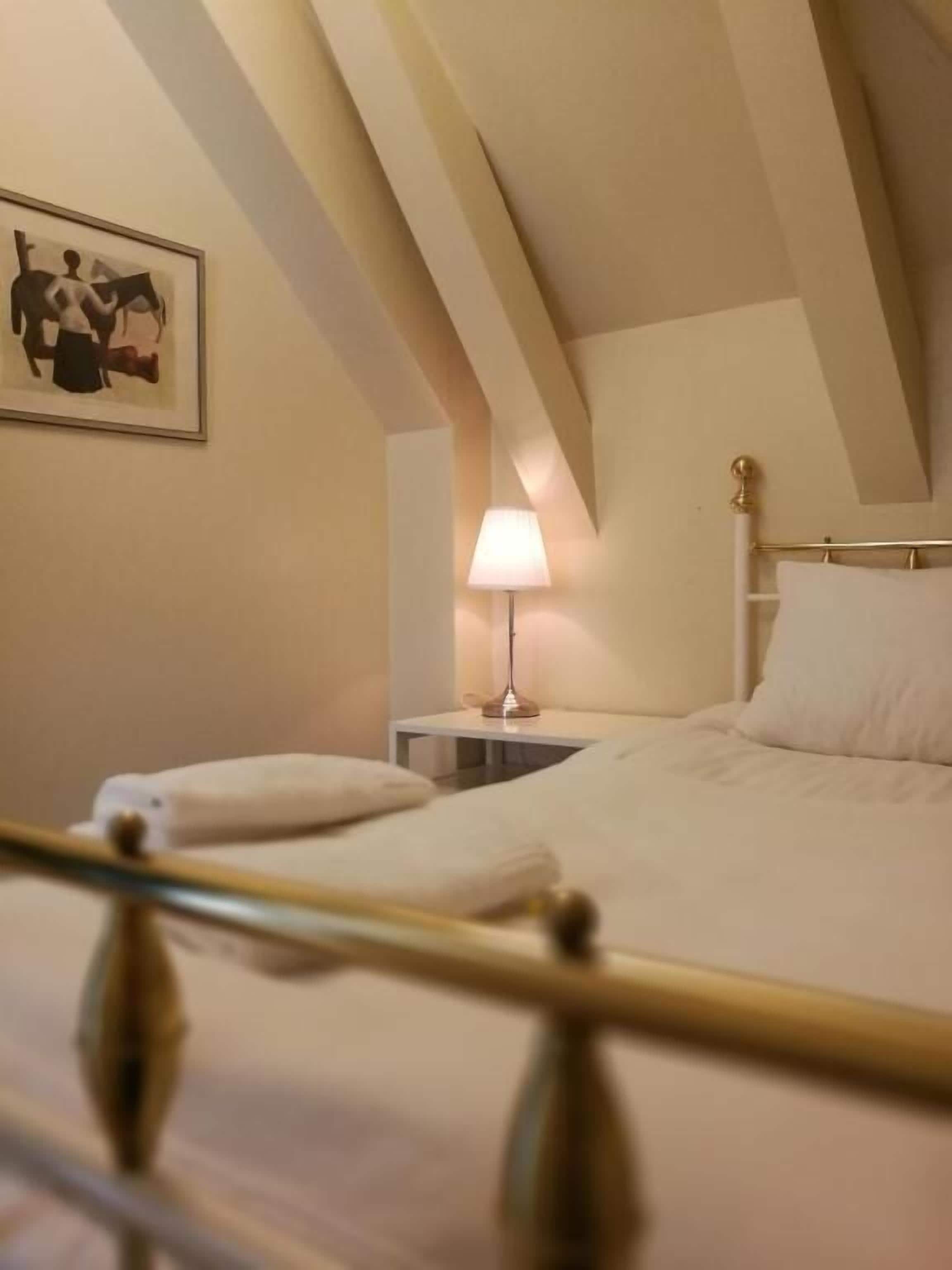 A neatly made bed with white linens, a bedside lamp, and a framed artwork on the wall.