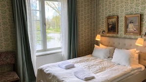 Een hotelkamer met een bed, twee wandlampen, een raam met gordijnen en twee ingelijste foto’s aan de muur.