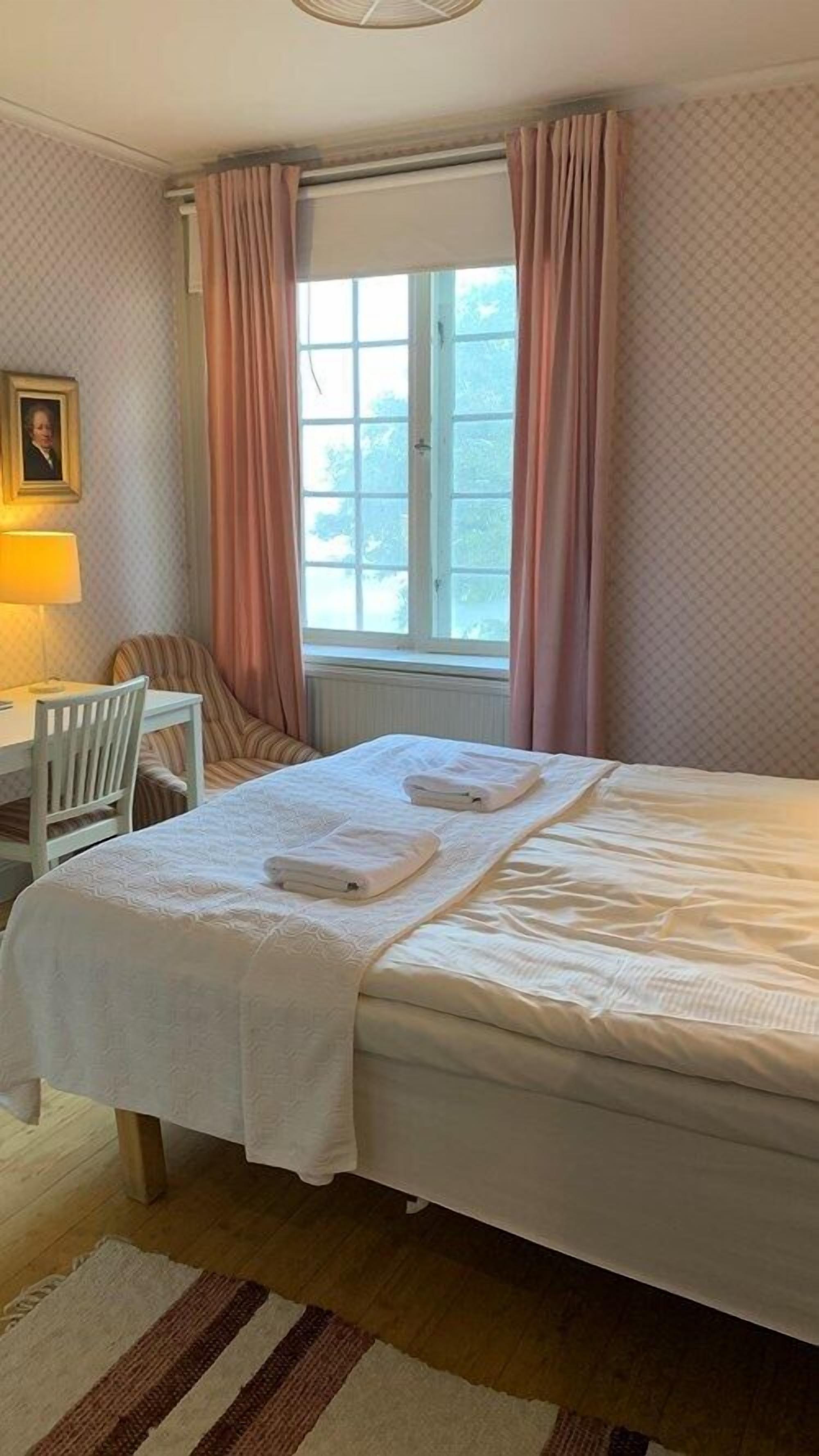 A neatly arranged bedroom with a bed, a chair, a desk, and a window with curtains.