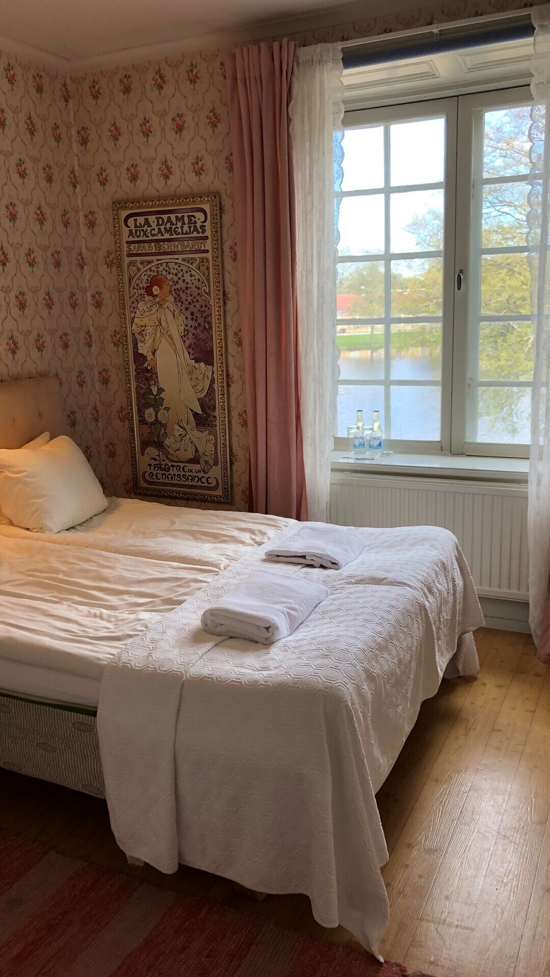 Une chambre à coucher avec un lit, une affiche, une fenêtre donnant sur un paysage et un radiateur.
