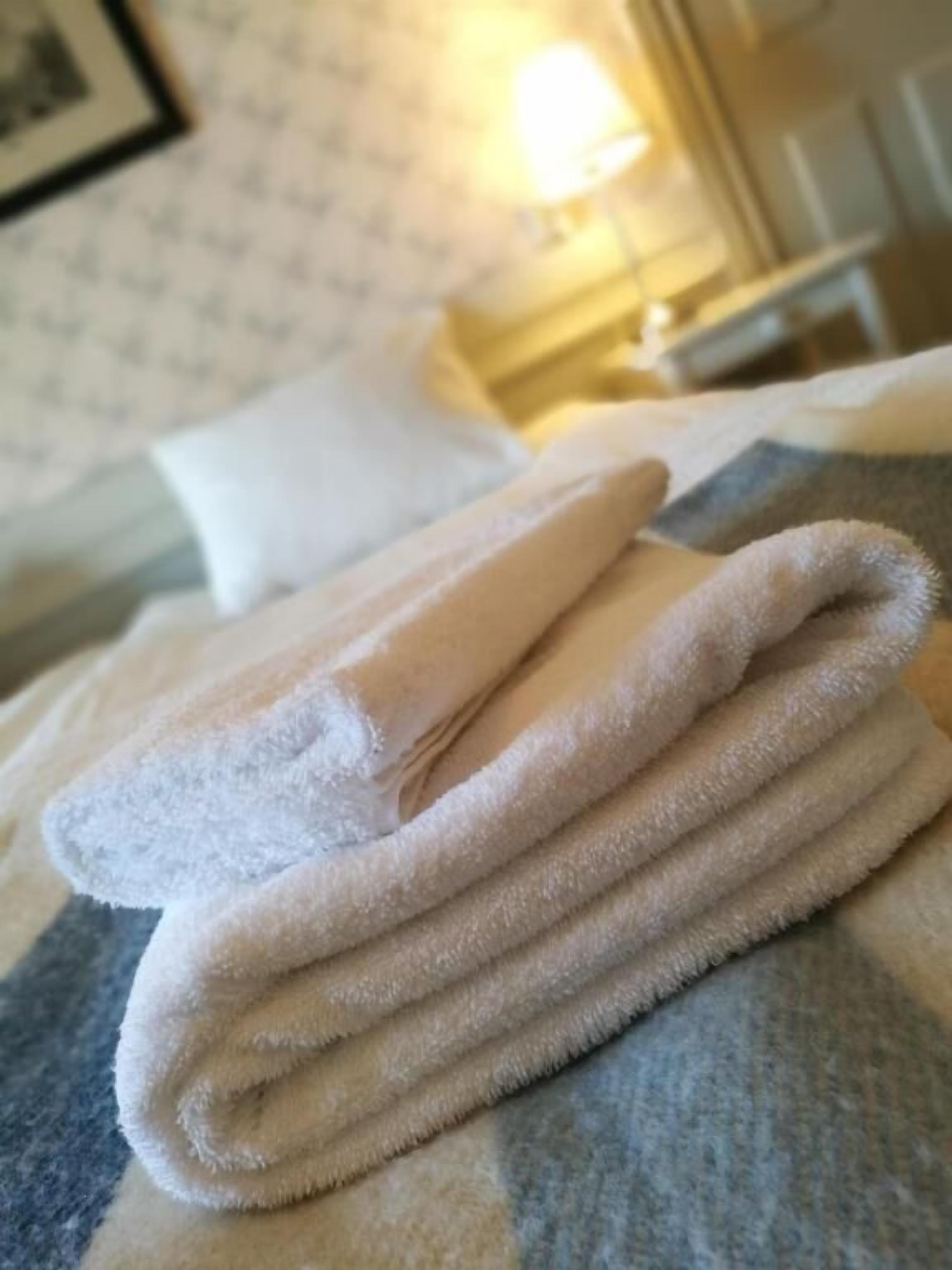 Ein ordentlich gefaltetes weißes Handtuch auf einem Bett mit einem gemusterten Bettbezug.