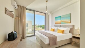 A modern hotel room with a large bed, a desk, a hanging light fixture, and a view of the outdoors. - Beach Sand Villa 2 - Beachfront Roof Pool Seaviews (Pirgos Psilonerou)