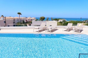 A pool with lounge chairs and a view of the sea.