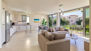 A modern kitchen with white cabinets, a dining area with a table and chairs, and a large window offering a view of the outside. - Beach Sand Villa 2 - Beachfront Roof Pool Seaviews (Pirgos Psilonerou)