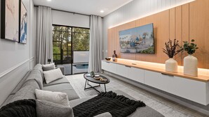 Una sala de estar moderna con un sofá gris, una mesa de centro y un televisor montado en una pared de madera.